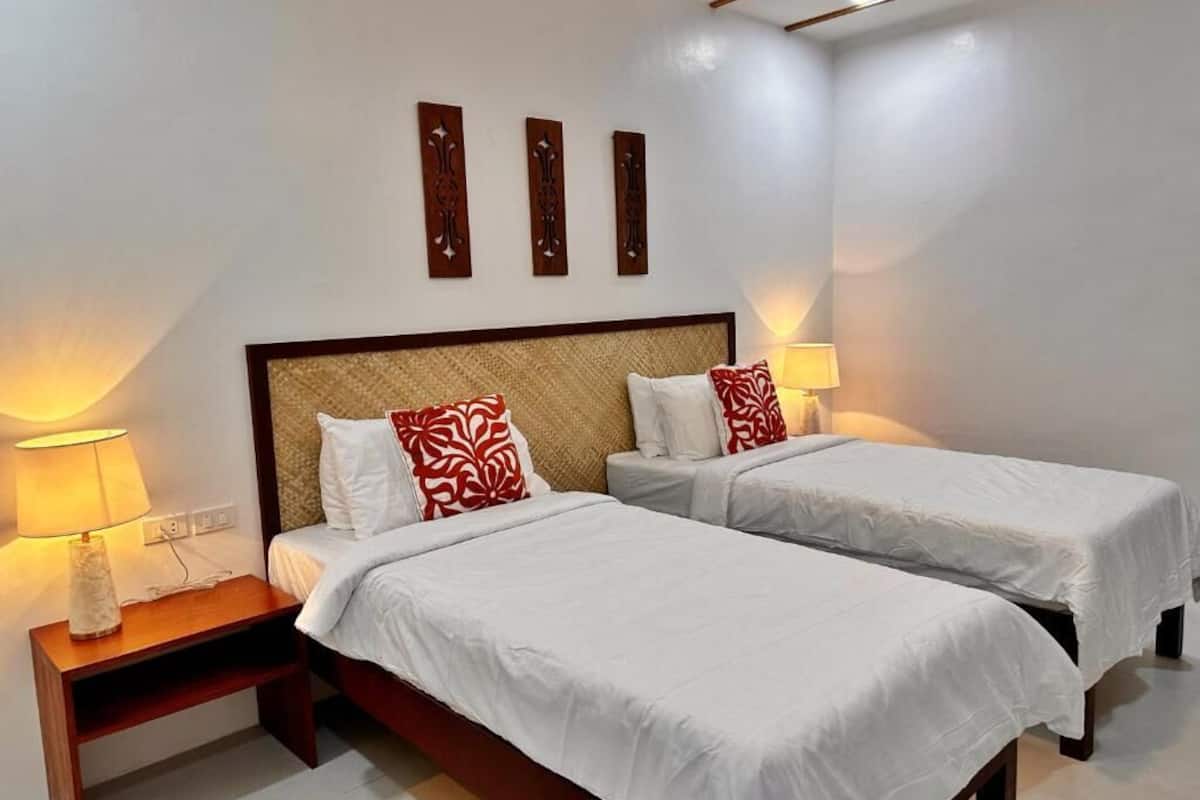 Habitación de hotel con dos camas individuales, una mesita de noche con lámpara y decoración en la pared.