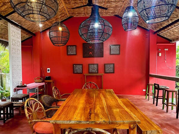 Un coin repas avec une table en bois, des chaises en osier et des lampes en osier suspendues au plafond.