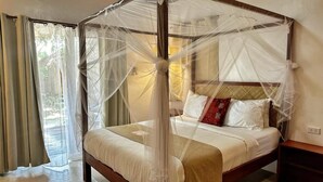 Una cama con dosel sostenido por cuatro columnas, con estructura de madera, ropa de cama blanca y una mesita de noche con lámpara.