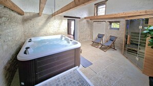 Een wellnessruimte met een bubbelbad, twee loungestoelen en een glazen deur naar buiten.