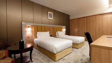 A hotel room with two beds, a desk, a chair, and a small table.