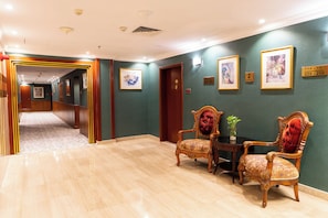 Un vestíbulo de hotel con un largo pasillo, dos sillones decorativos, una mesita con un florero y obras de arte en las paredes.