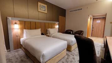 Habitación de hotel con dos camas, cabecero de madera, un cuadro en la pared y una puerta a la derecha.