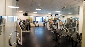 Un gimnasio con diversas máquinas de ejercicio, un espejo grande y un televisor en la pared.