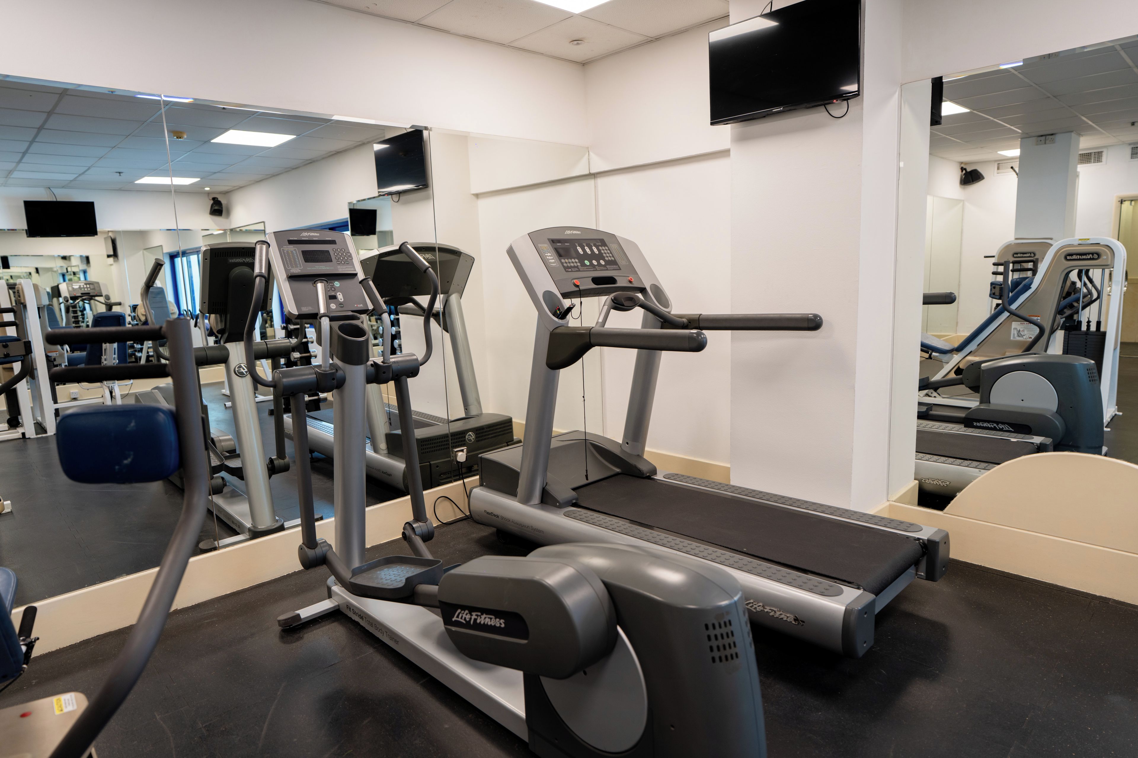 Gimnasio con equipo de cardio, máquinas de pesas y un espejo grande.