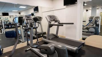 Gimnasio con equipo de cardio, máquinas de pesas y un espejo grande.