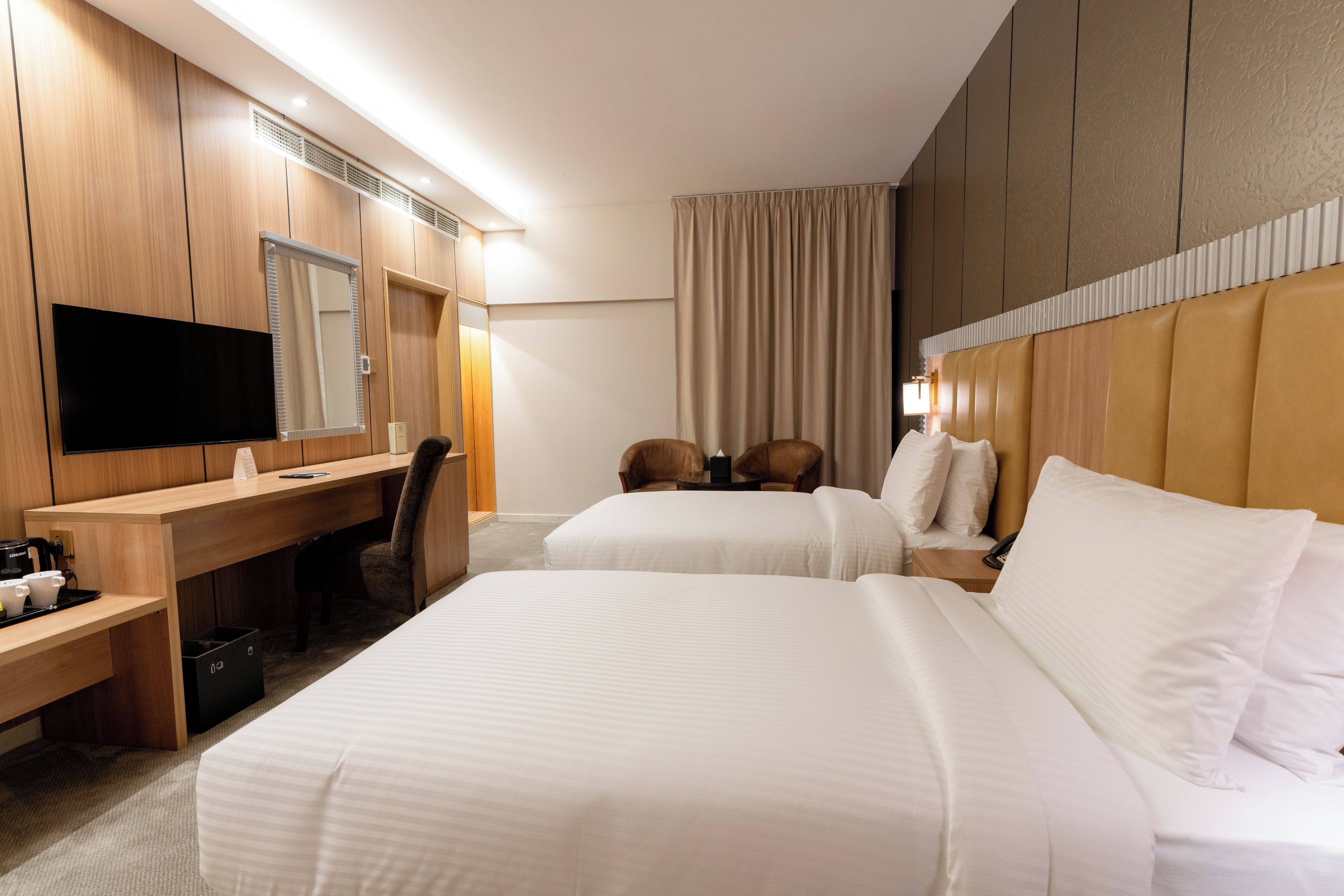 A hotel room with two beds, a desk, a chair, a television, and a large mirror.