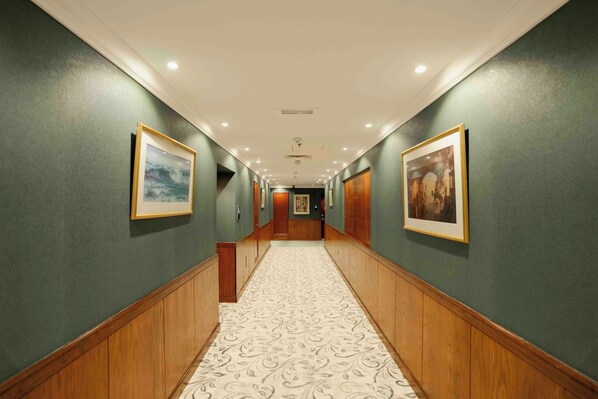A hallway with green walls, wooden paneling, and patterned carpet.