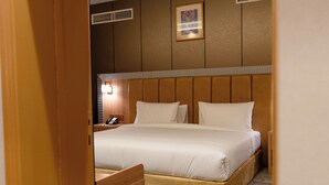 Habitación de hotel con una cama grande, una mesita de noche con lámpara, un cuadro enmarcado en la pared y piso alfombrado.