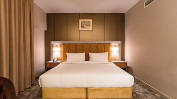 A hotel room with a large bed, two bedside tables with lamps, a headboard, and a picture on the wall.