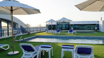 A poolside area with lounge chairs and umbrellas, a glass-enclosed structure, and a blue railing.