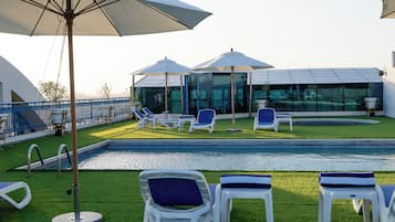A poolside area with lounge chairs and umbrellas, a glass-enclosed structure, and a clear view of the sky.