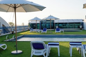 A poolside area with lounge chairs and umbrellas, a glass-enclosed structure, and a clear view of the sky.