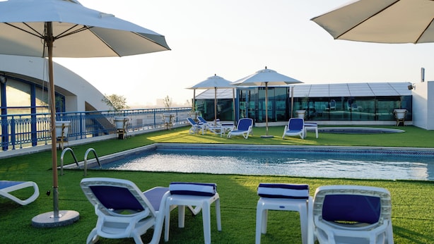 Zona junto a la piscina con sillones de descanso y sombrillas, una estructura de cristal y una baranda azul.