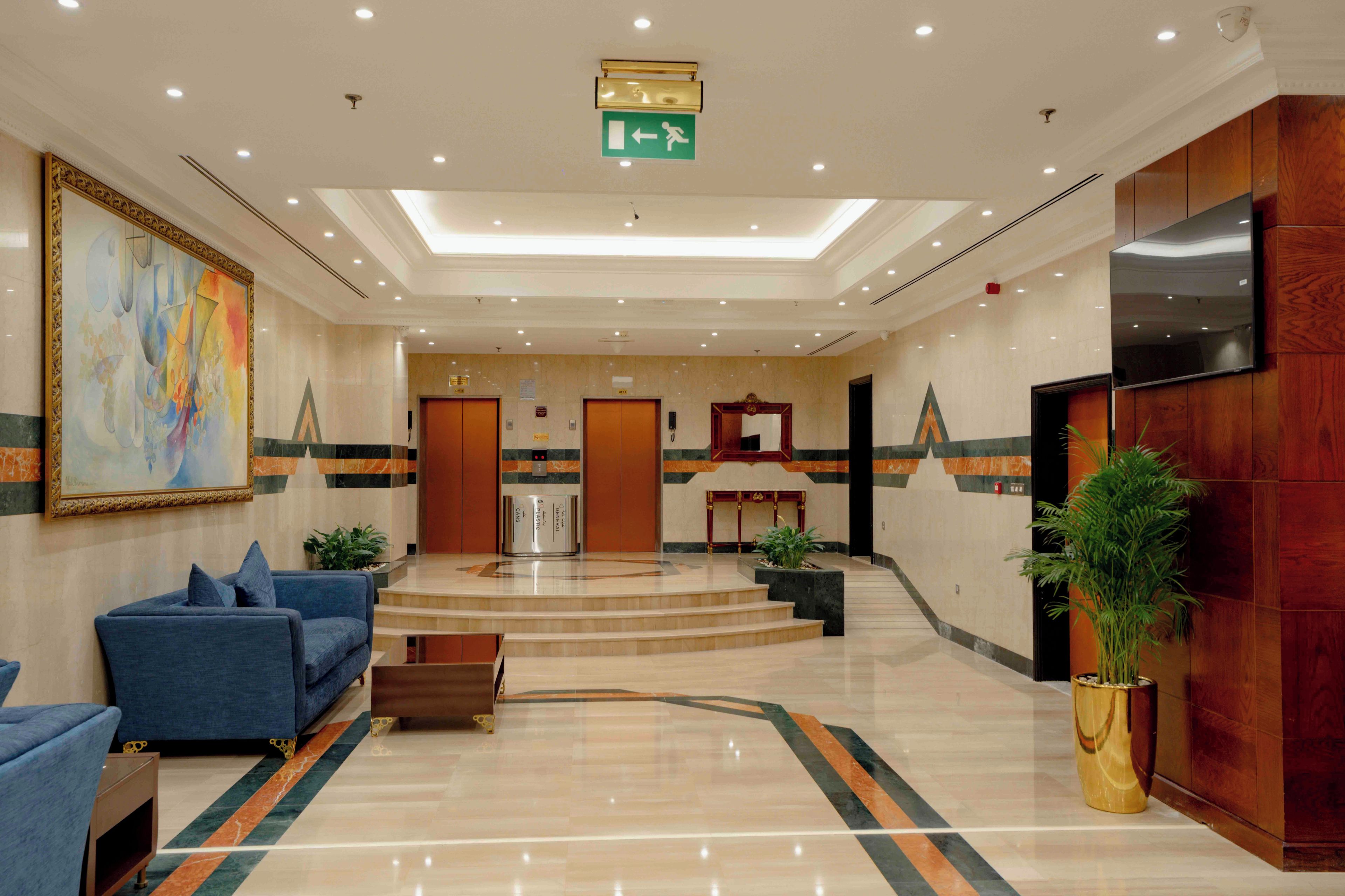 Eine Hotellobby mit einer Rezeption, zwei Aufzügen, einem blauen Sofa und einem großen Gemälde an der Wand.