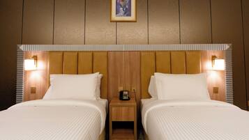Une chambre d’hôtel avec deux lits, une tête de lit en bois, des lampes de chevet, une petite table de chevet en bois avec un téléphone et un tableau encadré au mur.