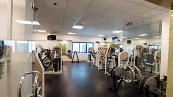A gym with various exercise machines, a large mirror, and a television on the wall.