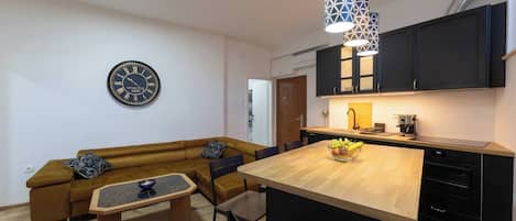 A modern kitchen with a wooden island, black cabinets, and a clock on the wall.