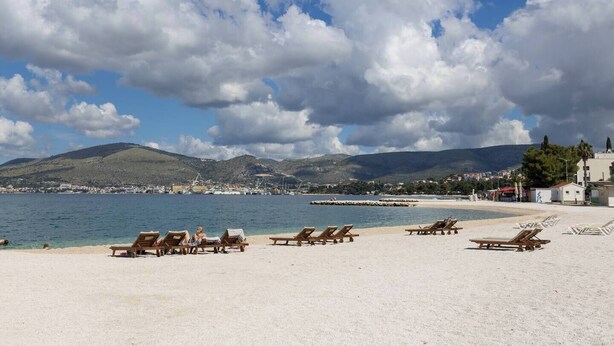 Une plage avec des chaises longues, un ciel dégagé et une vue lointaine sur une ville et des montagnes.