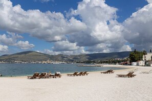 A beach with lounge chairs, a clear sky, and a distant view of a town and mountains.
