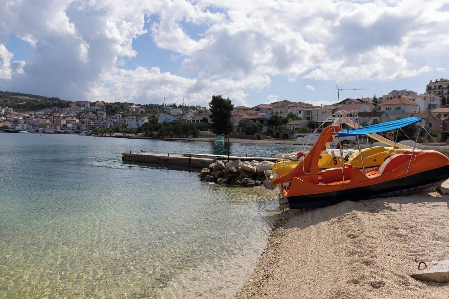 Una playa con agua cristalina, una orilla de arena y un pequeño bote naranja con toldo azul.