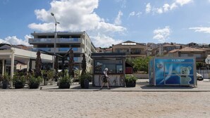 Une place publique avec un kiosque, un bâtiment moderne et une enseigne indiquant la présence d’une boutique de glaces.