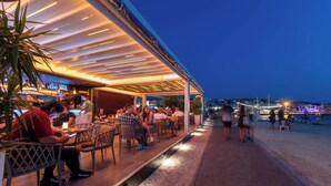 Un espace de restauration en plein air avec des tables et des chaises, un bar en arrière-plan et une vue sur la mer.