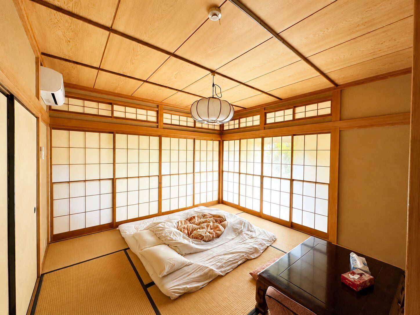 A traditional Japanese room with tatami flooring, a futon bed, a dark wooden table, and shoji screens.