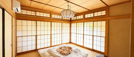 A traditional Japanese room with tatami flooring, a futon bed, a dark wooden table, and shoji screens.