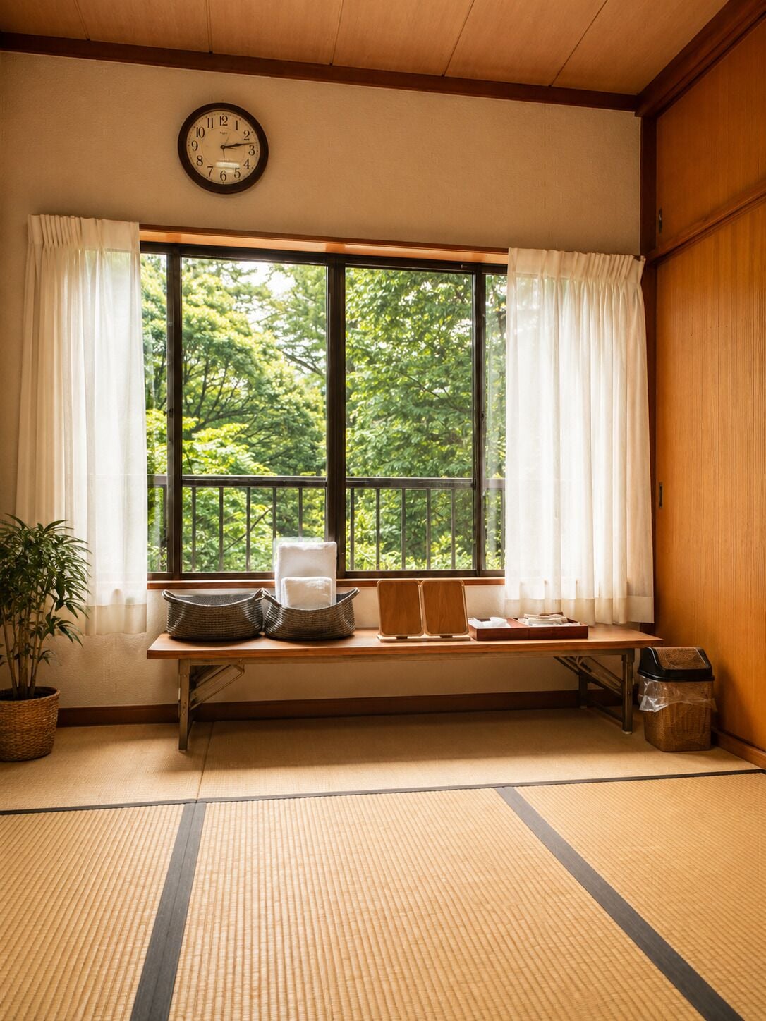 Una habitación con suelo de tatami, un banco de madera, un reloj y una ventana que da a un paisaje de árboles.