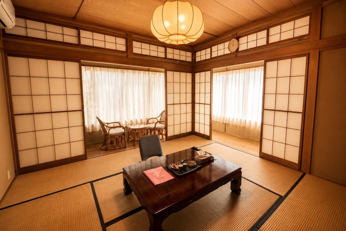 Perinteinen japanilainen huone, jossa on tatamimatto, puinen pöytä ja shoji-tyylinen liukuoviseinä.