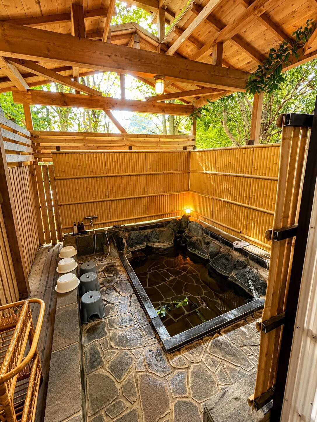 A traditional Japanese onsen with a stone hot spring, wooden walls, and a bamboo fence.