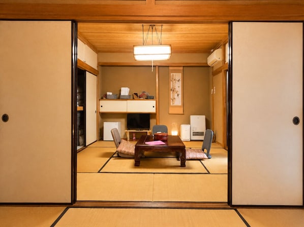 Ett traditionellt japanskt rum med tatamimattor på golvet, ett lågt bord med kuddar, en tv och en värmare.