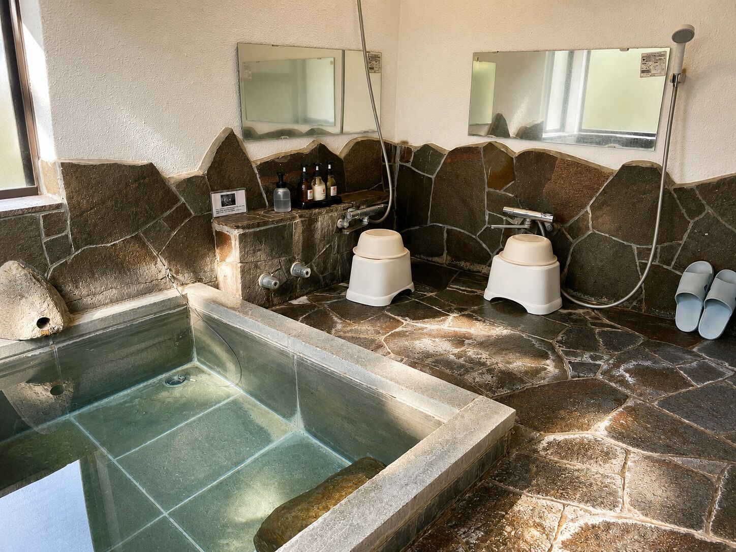 A stone-walled bathroom with a bathtub, two sinks, and a shower.
