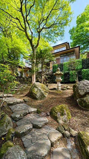 A traditional Japanese garden with stone pathways, a stone lantern, and a building in the background. - KUMO INN (Hakone)