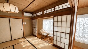 Una habitación japonesa tradicional con suelo de tatami, puertas correderas, una lámpara colgante y una silla de mimbre.