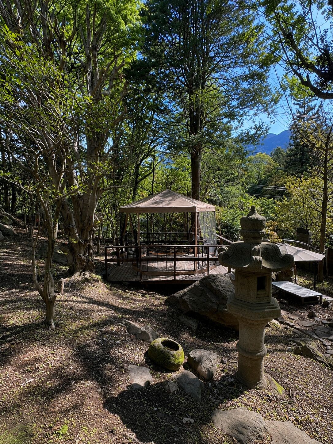 A traditional Japanese garden with a wooden gazebo, stone lanterns, and a stone bridge.