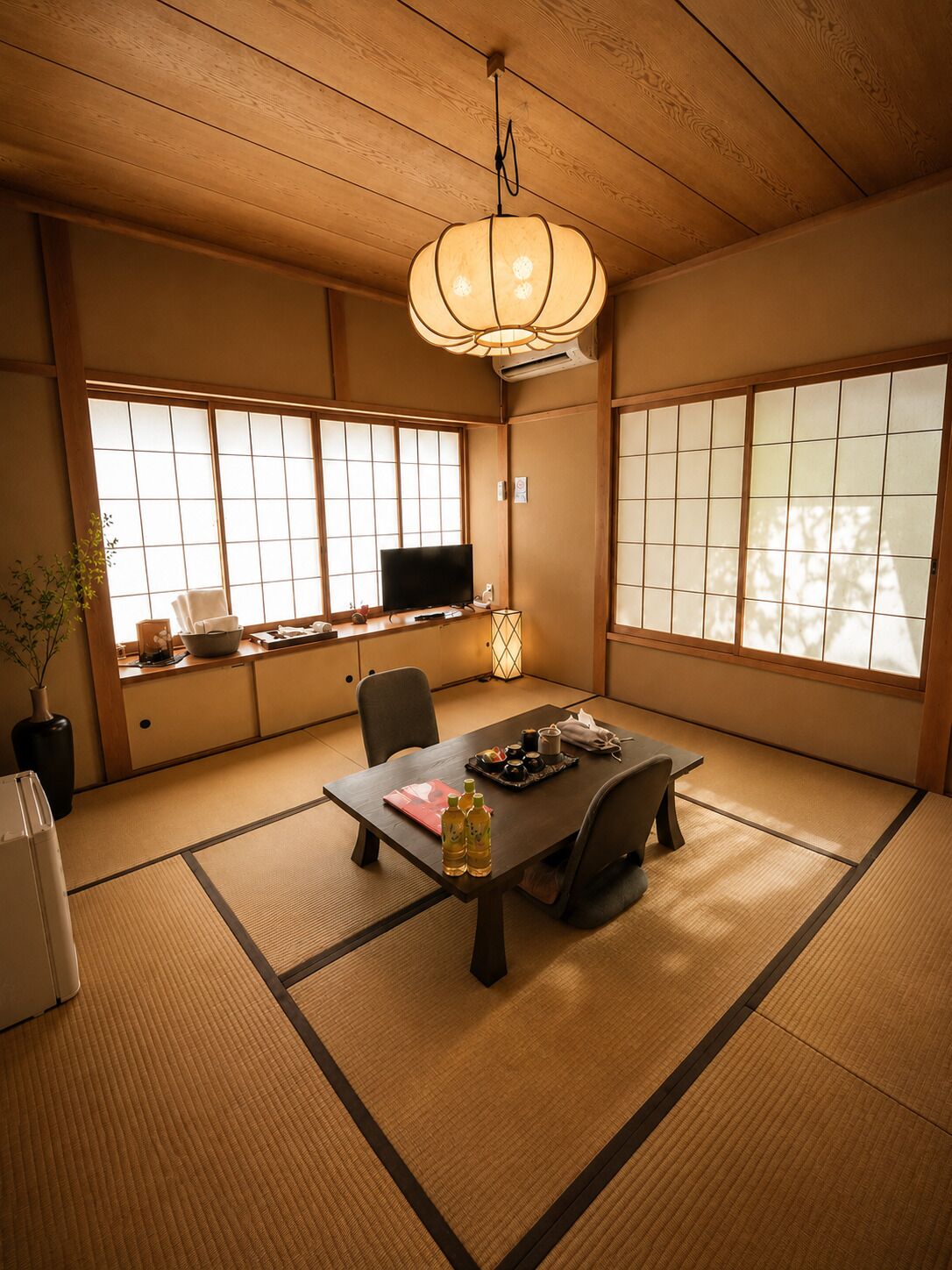 Una habitación tradicional japonesa con suelo de tatami, una mesa baja con televisor y puertas correderas.