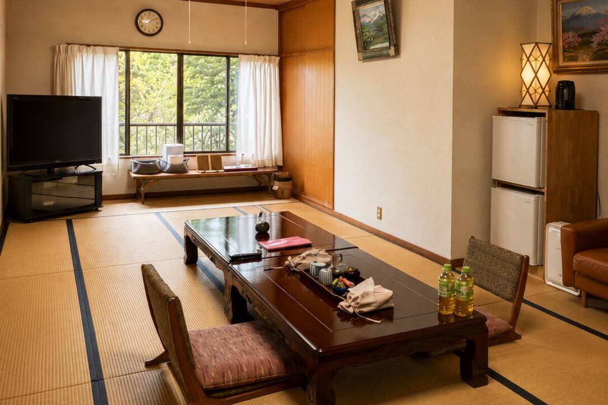 Una habitación de estilo japonés tradicional con suelo de tatami, una mesa baja, televisión y vistas a zonas verdes.