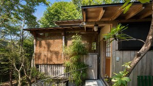 Un edificio tradicional japonés de madera, con un sendero de piedra que lleva a la entrada y una planta de bambú al frente.