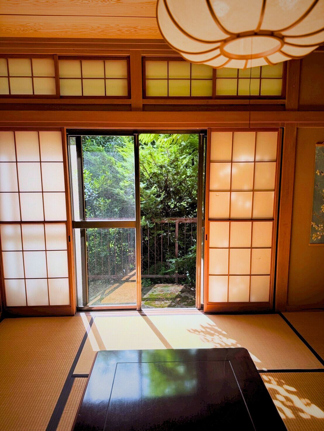 Una habitación japonesa tradicional con suelo de tatami, puertas correderas y vistas a un jardín.