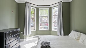 A bedroom with a bed, a dresser, and a bay window with curtains. - Spacious flat in the heart of Tottenham (London)