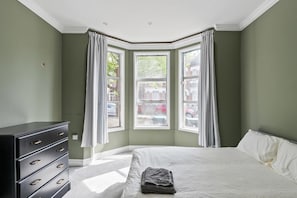Ein Schlafzimmer mit einem Bett, einer Kommode und einem Erkerfenster mit Vorhängen.