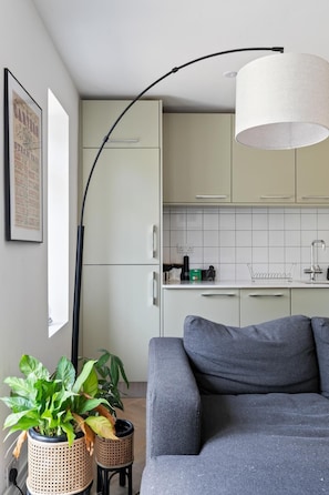 Eine moderne Küche mit weißen Schränken, einer schwarzen, gebogenen Leuchte und einem grauen Sofa.