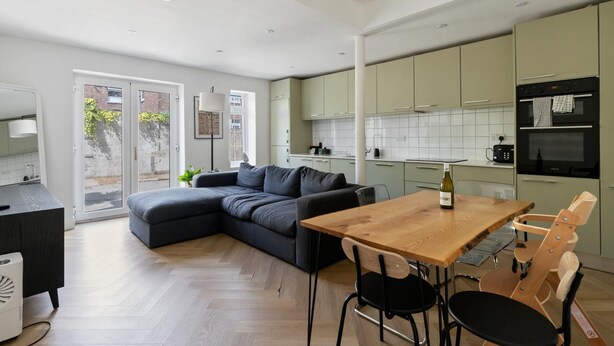 A modern kitchen with green cabinets, a wooden dining table, and a black chair. - Spacious flat in the heart of Tottenham (London)