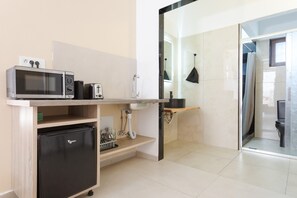 Een kleine keuken met een magnetron, broodrooster en koelkast, een spoelbak en een douchecabine met glazen wanden.