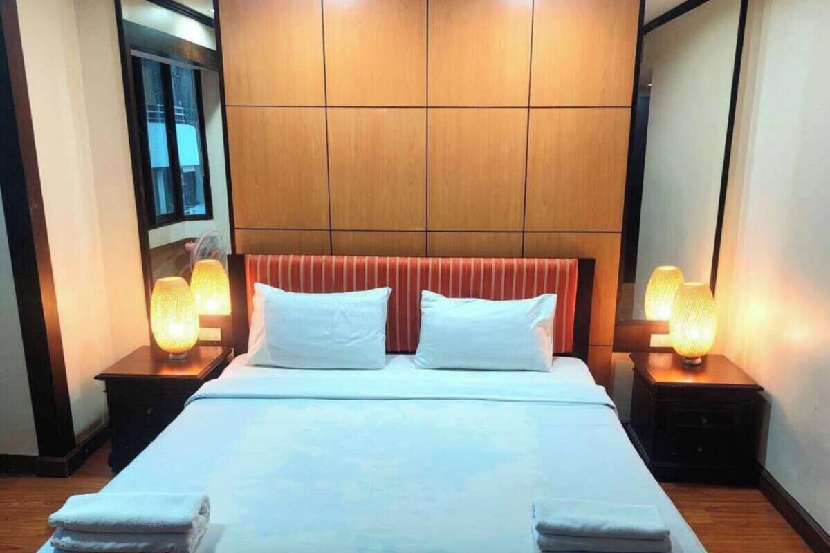 A neatly made double bed with white linens, two bedside lamps, and a wooden headboard.