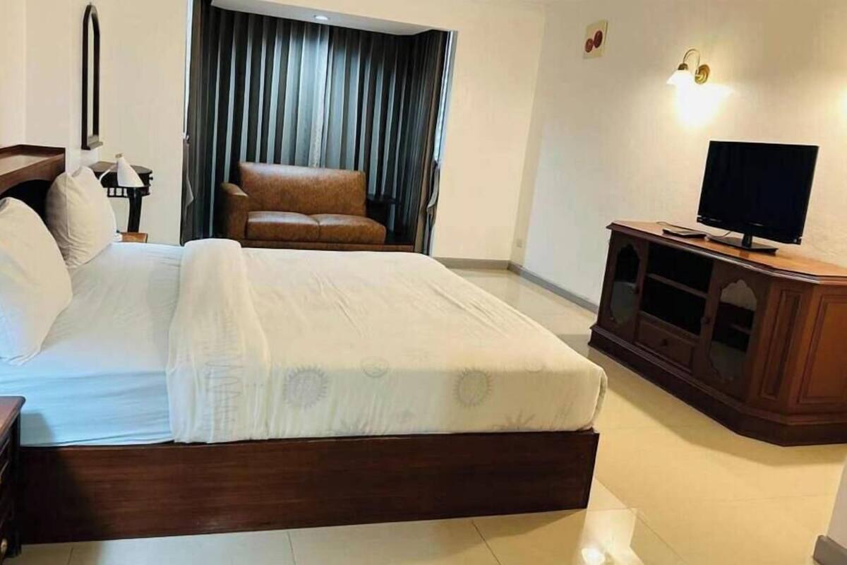 A hotel room with a large bed, a television, a desk, and a sofa.