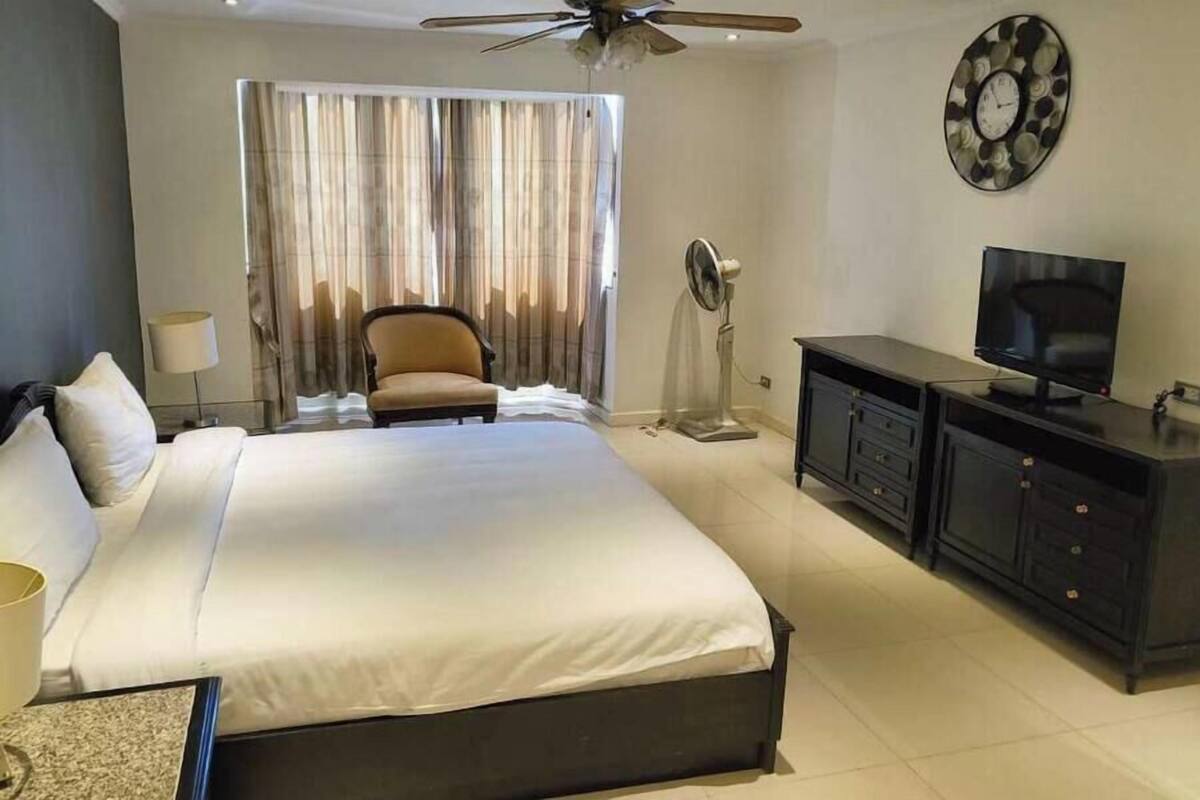 A hotel room with a bed, a chair, a TV, a desk, and a ceiling fan.