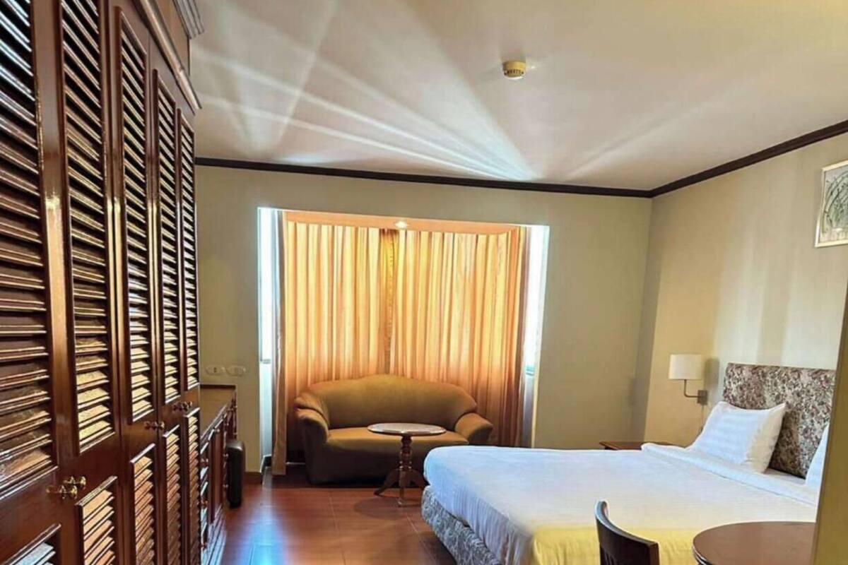A hotel room with a bed, a chair, a small table, a sofa, and a window with curtains.